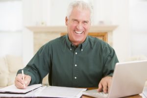 Man in dining room with laptop and paperwork smiling